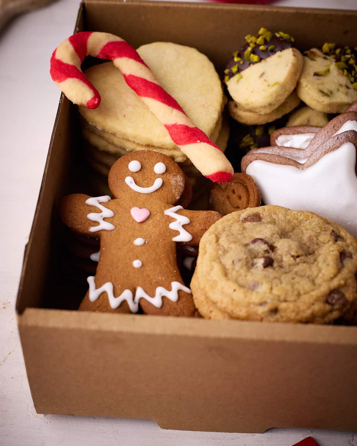 A close up of inside the cookie box, displaying a gingerbread man, chocolate chip cookies, iced gingerbread stars, heart sugar cookies, pistachio shortbread cookies, and a candy cane cookie.