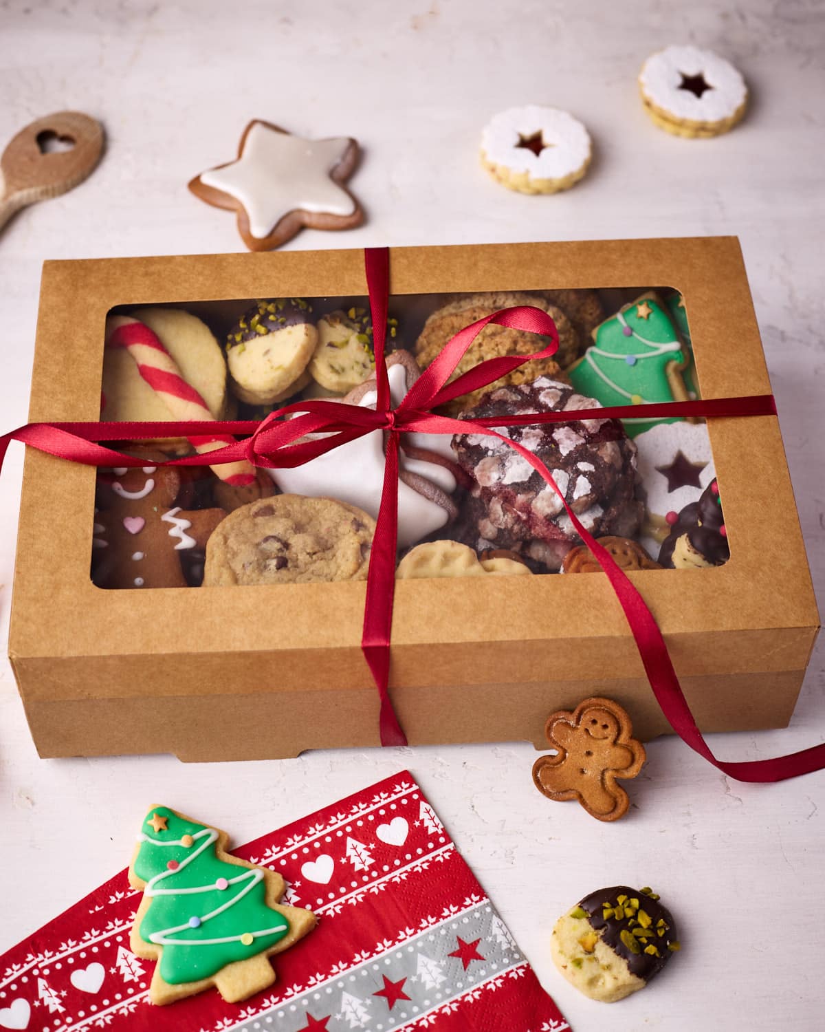 Christmas cookie box wrapped in red ribbon, with a few cookies dotted around it.