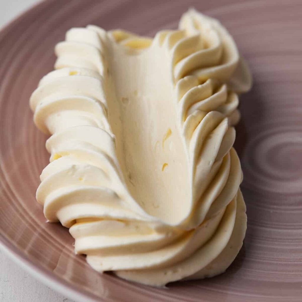 Buttercream piped in a swirl on a plate with a swipe pulled through it to show its smooth texture after being fixed from broken buttercream.