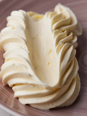 Buttercream piped in a swirl on a plate with a swipe pulled through it to show its smooth texture after being fixed from broken buttercream.