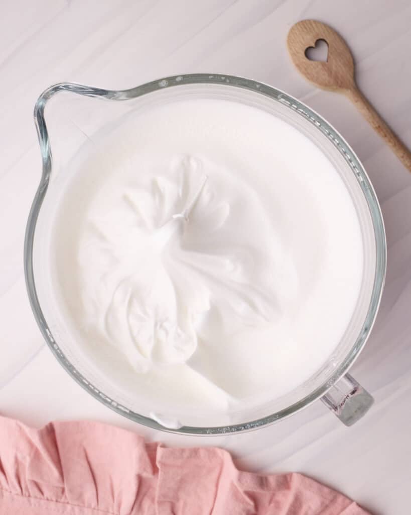 Meringue in a glass mixing bowl, whipped to firm peaks to make angel food cake.