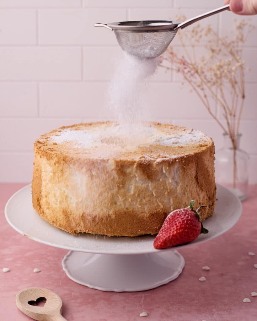 Action shot of powdered sugar being sifted on top of an angel food cake.