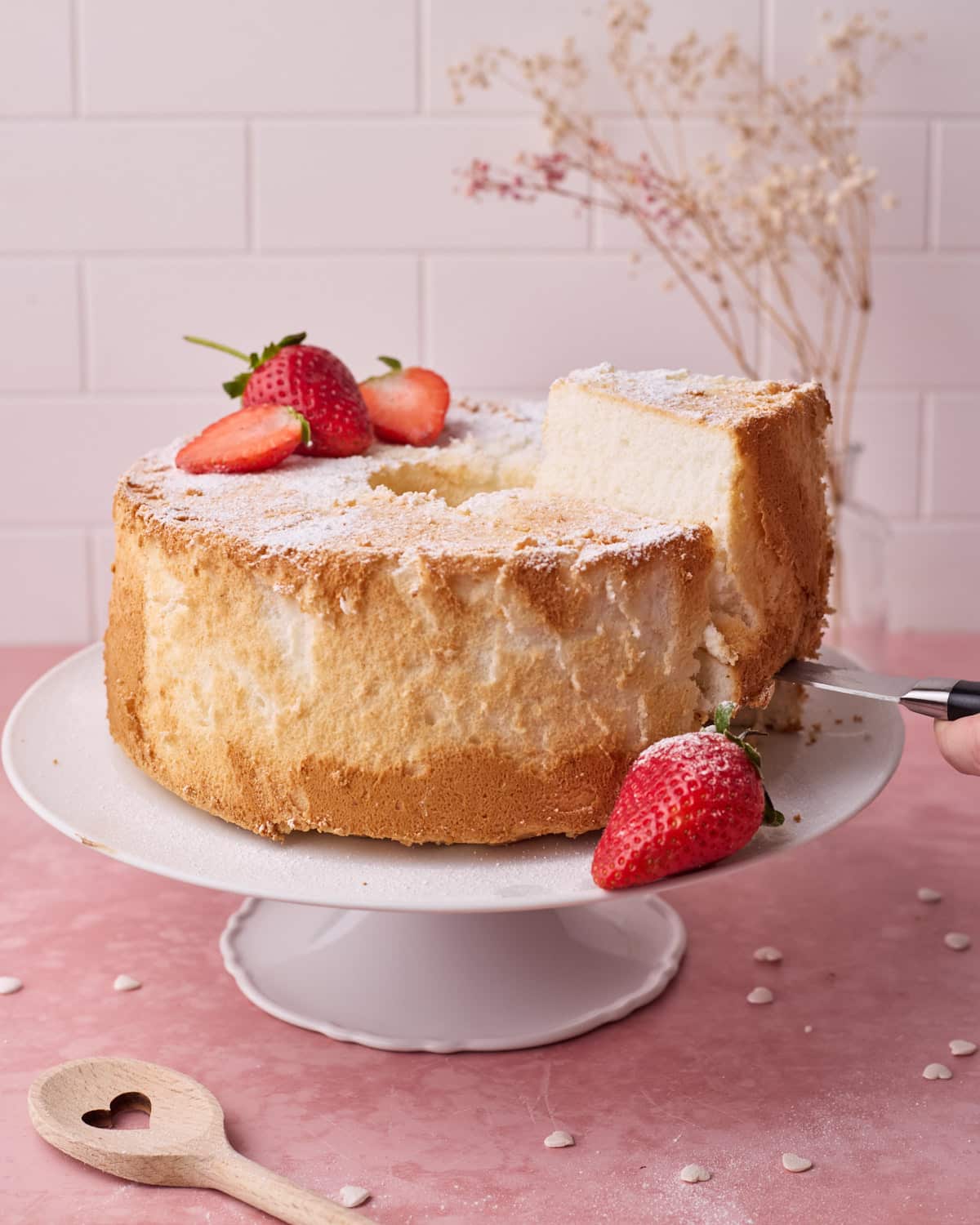 Angel food cake on a white cake stand with a slice being taken out of it.