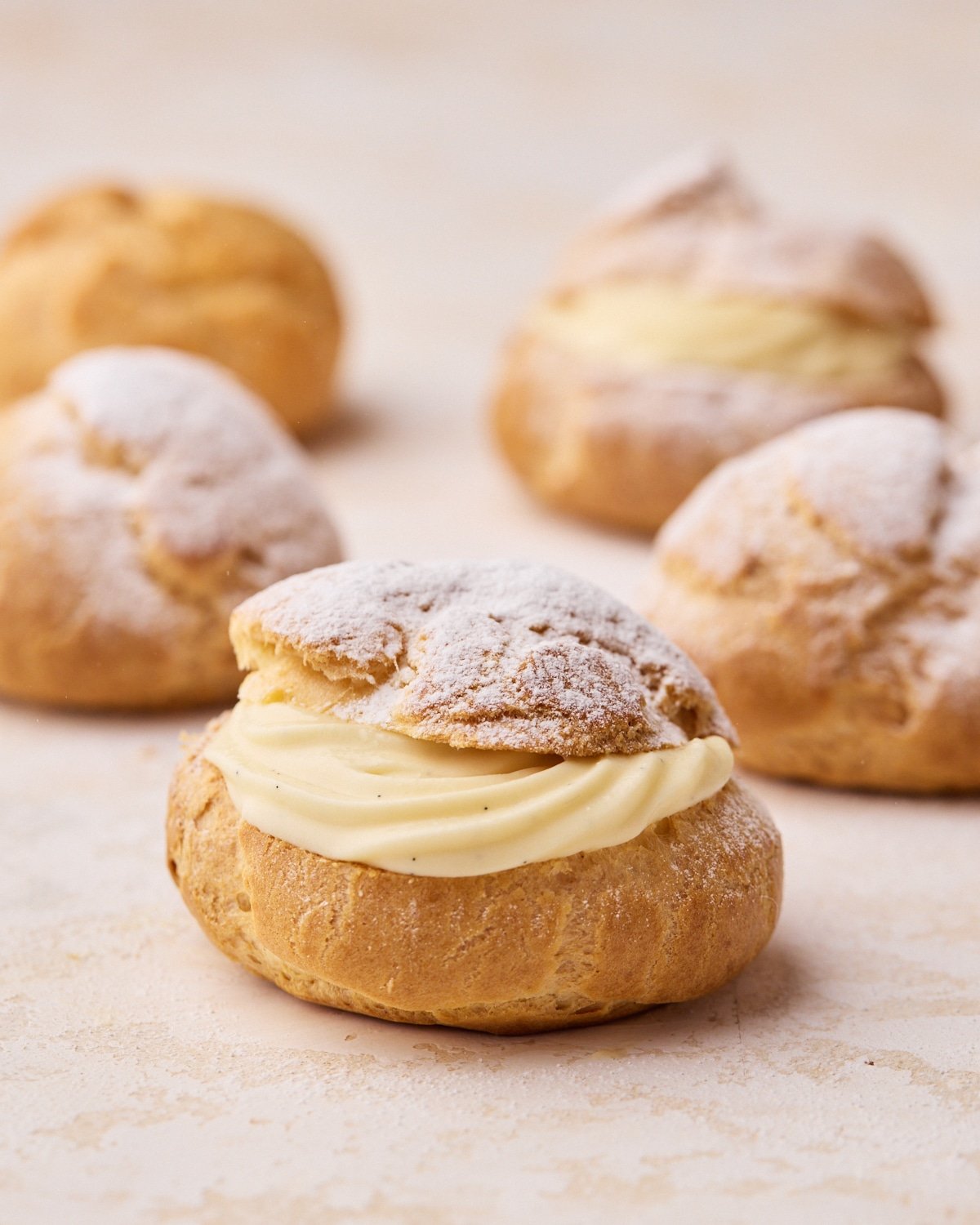 Homemade cream puffs being dusted with icing sugar.