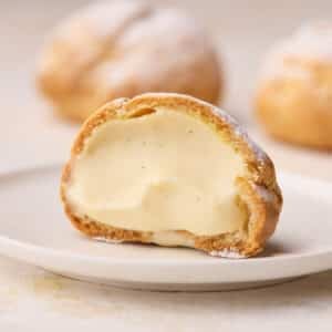 A single cream puff on a small plate, sliced open to show the creamy filling inside.