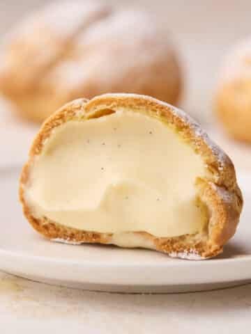 A single cream puff on a small plate, sliced open to show the creamy filling inside.
