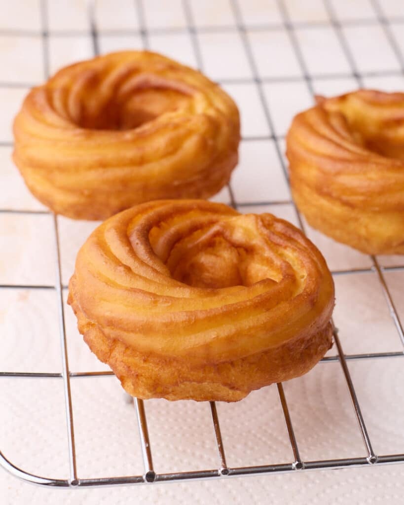 French crullers that have just been fried, sitting on a wire rack before they are glazed.