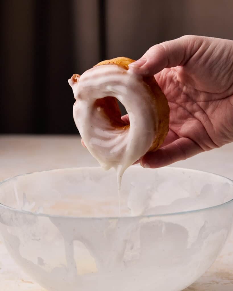 French cruller being dipped in vanilla glaze.