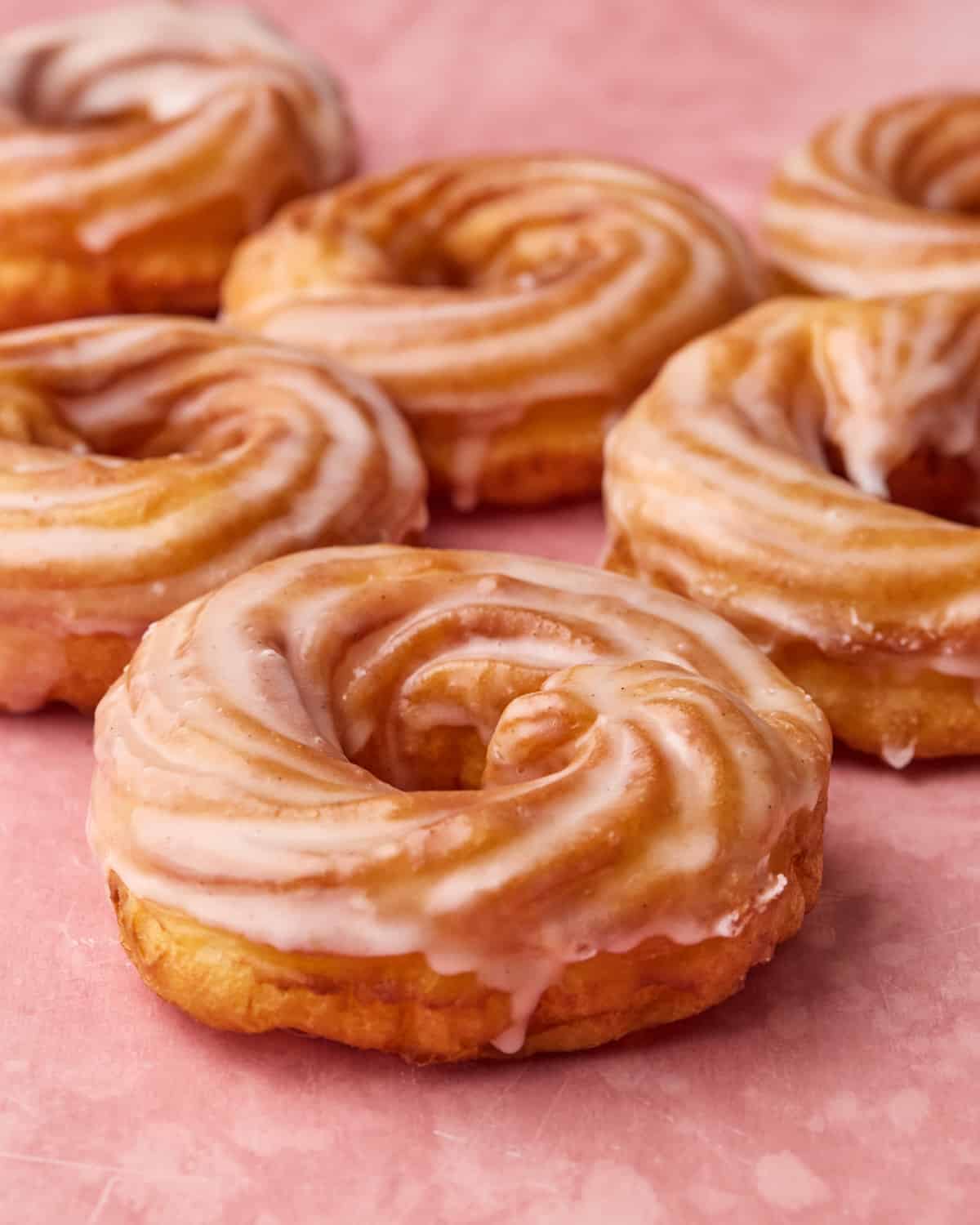A bunch of freshly made French cruller donuts on a pink backdrop.