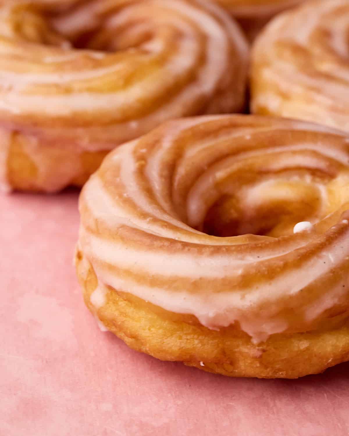 Close up of a French cruller showing the sharp ridges, swirl shape, and shiny glaze.