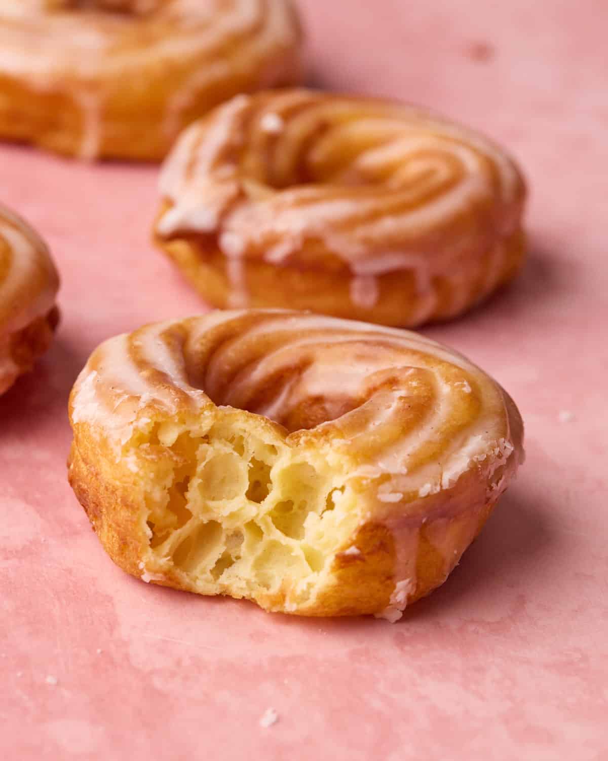 Close up of a french cruller with a bite taken out of it to show the honeycomb structure inside.