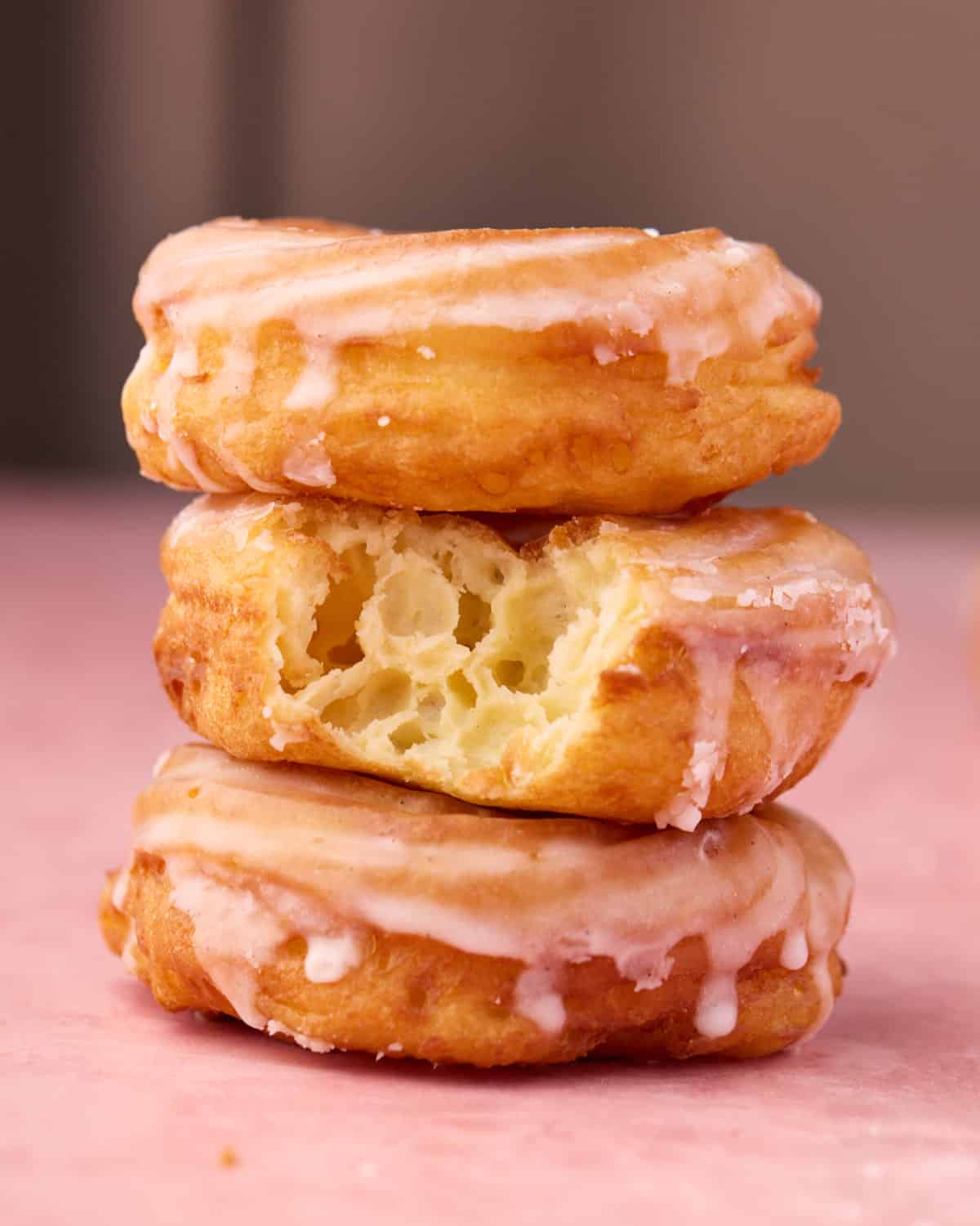 Stack of three cruller donuts, the middle one has a bite taken out of it to show the airy interior. 