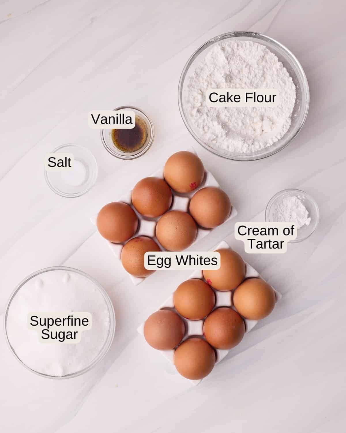 Ingredients to make angel food cake, including egg whites, sugar, cake flour, cream of tartar, vanilla, and salt.