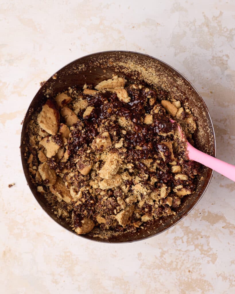 Crushed biscuits being stirred into melted chocolate mixture to make tiffin.