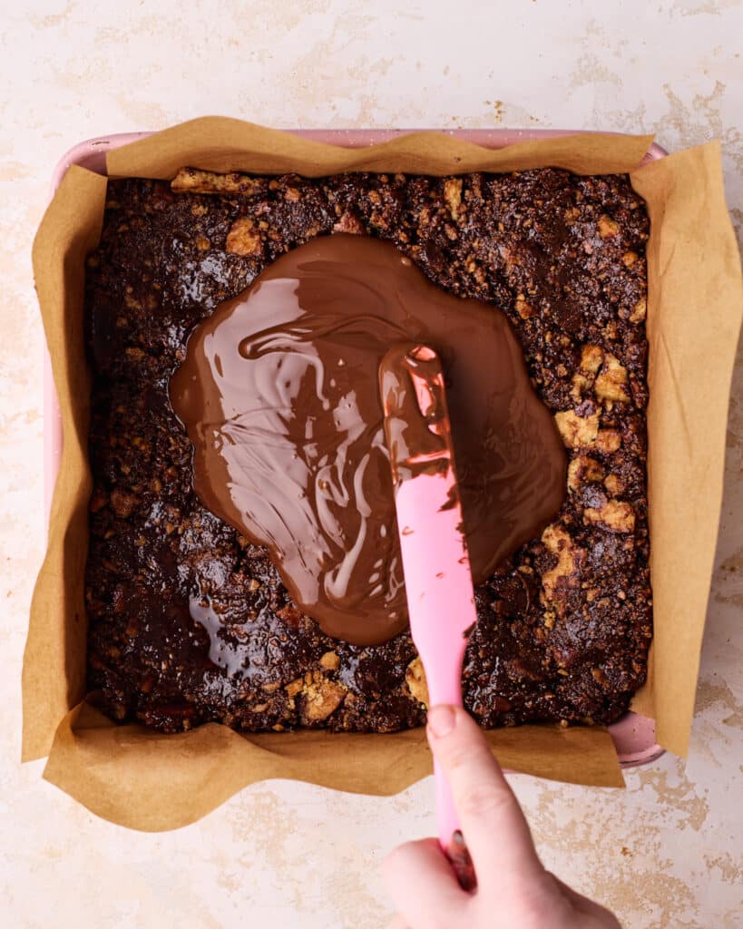 Melted chocolate being spread over chocolate tiffin in the pan.