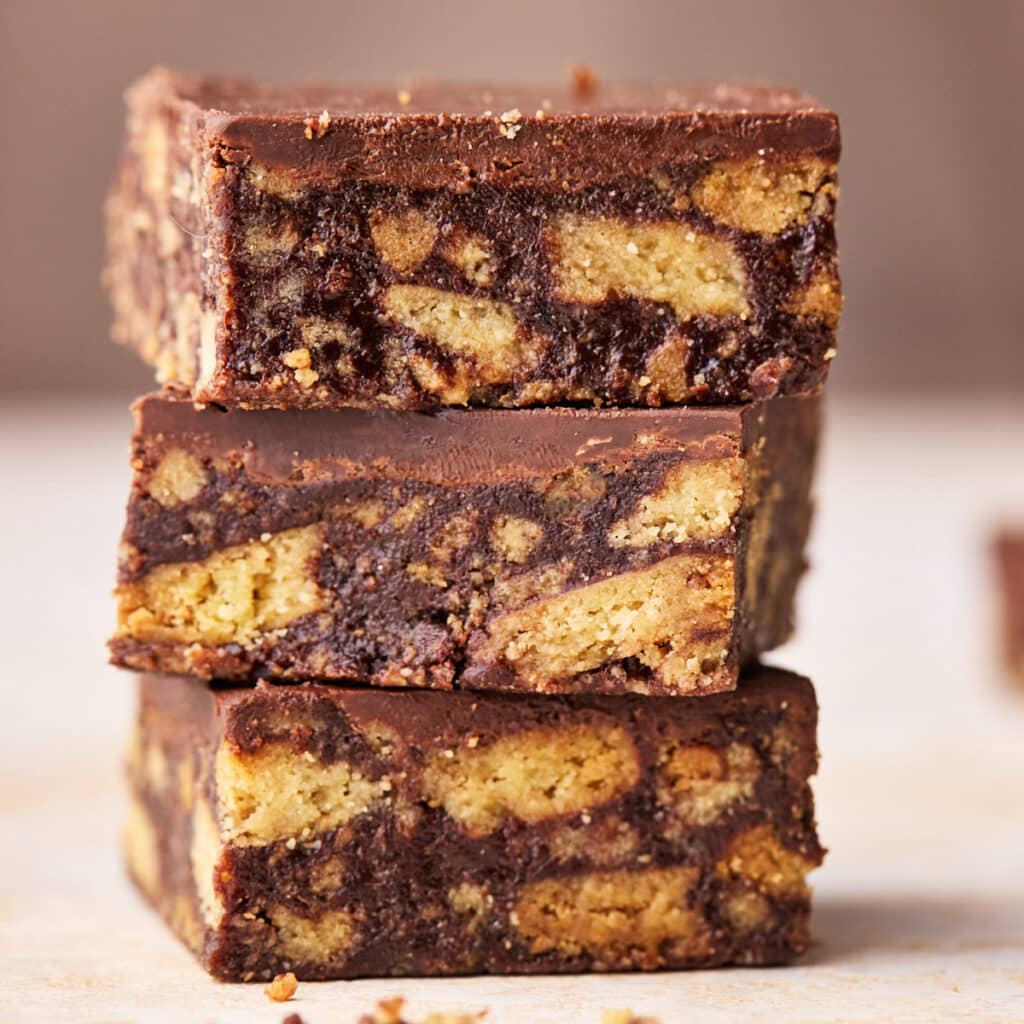 Three squares of Scottish tiffin in a stack, showing the insides with chunks of biscuit in a chocolate filling.