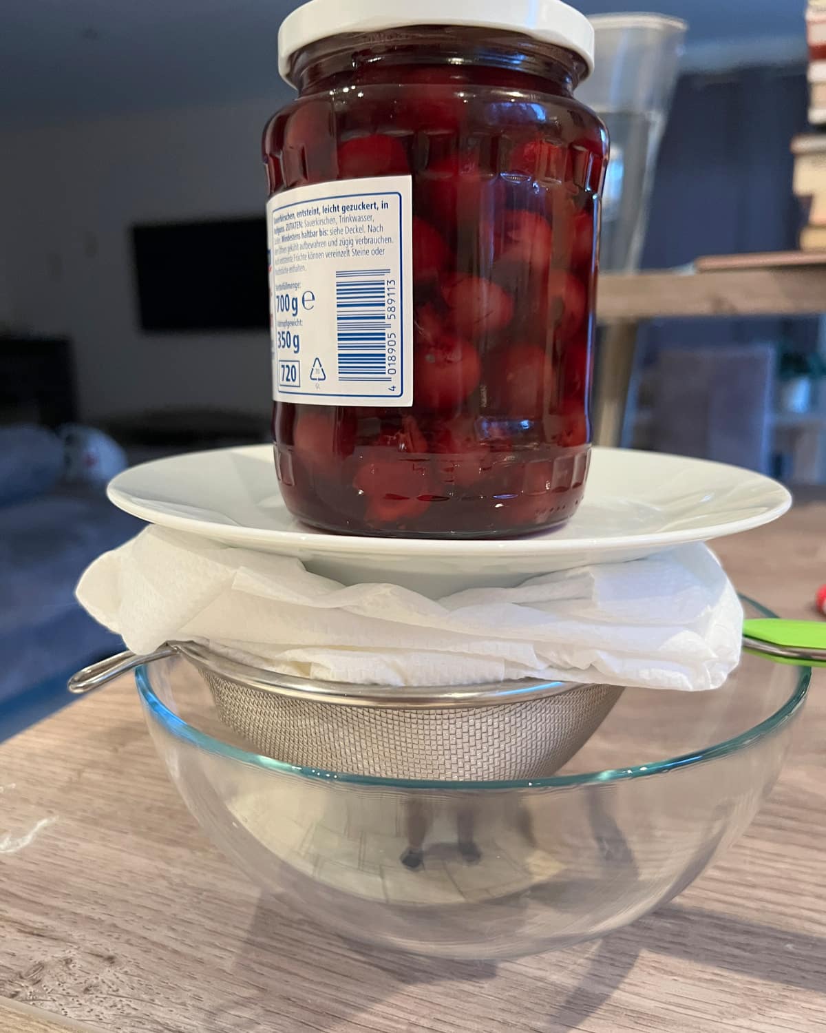 Ricotta cheese being strained through a cheesecloth with a heavy jar and plate on top to weigh it down.