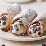 Three chocolate chip cannoli on a plate with homemade cannoli filling.