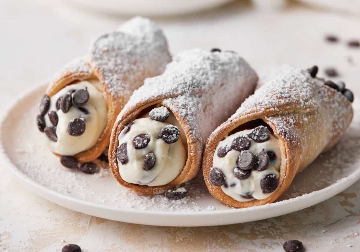 Three chocolate chip cannoli on a plate with homemade cannoli filling.