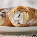 close up of a cannoli with a bite taken out to show the creamy filling inside.
