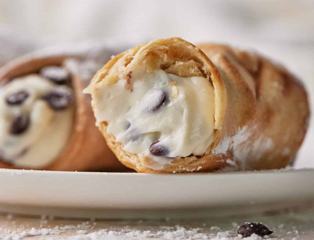 close up of a cannoli with a bite taken out to show the creamy filling inside.