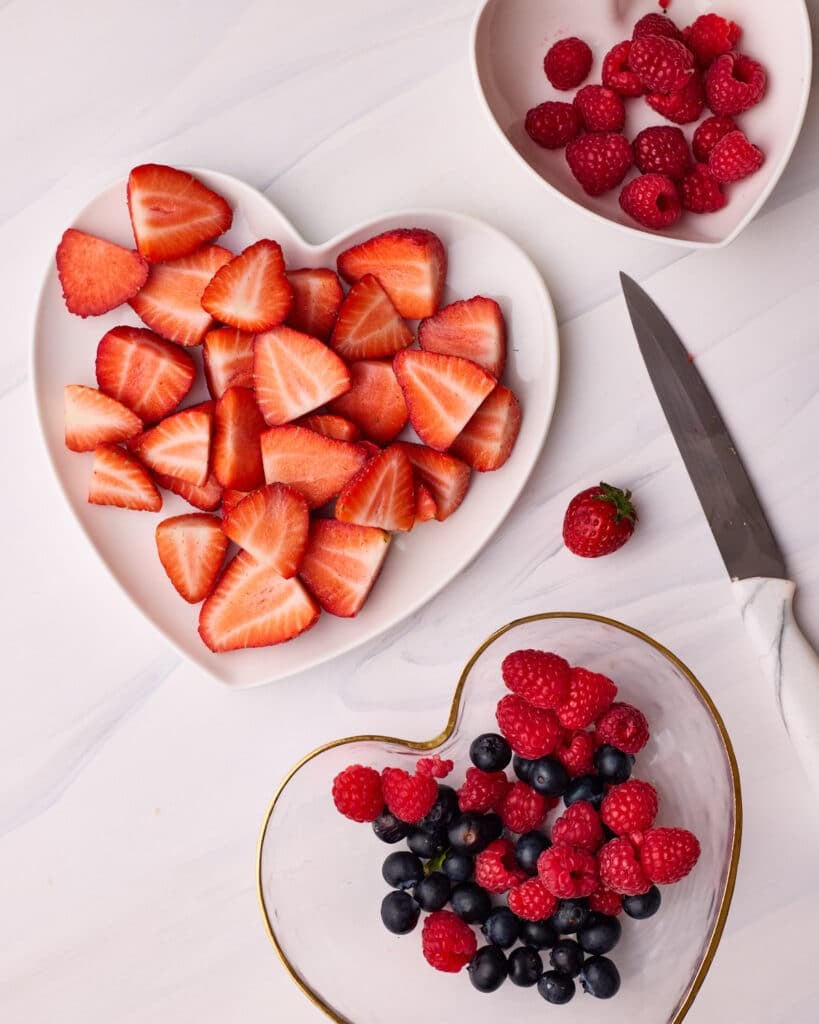 Fresh berries being sliced to go on top of a fresh fruit tart.