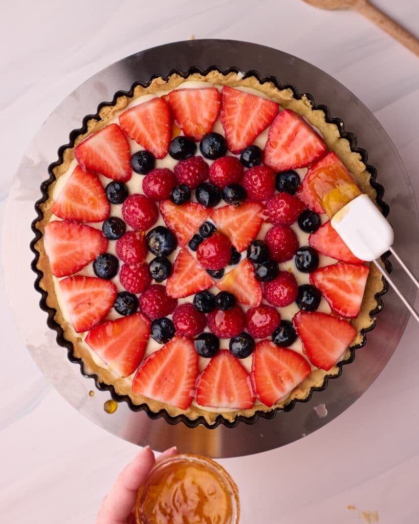Apricot jam being brushed onto berries on a fresh fruit tart to add a shiny glaze.