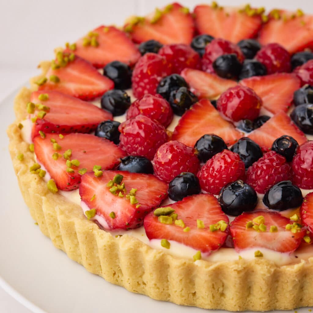 Fresh fruit tart in a shortbread crust with sliced strawberries, blueberries, and raspberries arranged in a pattern on top of pastry cream filling.