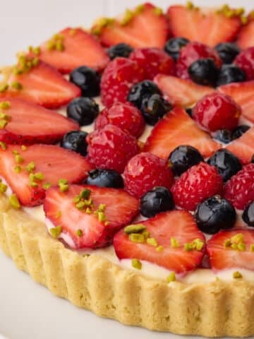 Fresh fruit tart in a shortbread crust with sliced strawberries, blueberries, and raspberries arranged in a pattern on top of pastry cream filling.