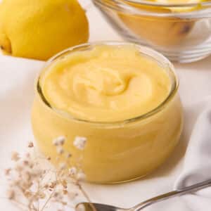Homemade lemon curd in a jar with fresh lemons surrounding it.