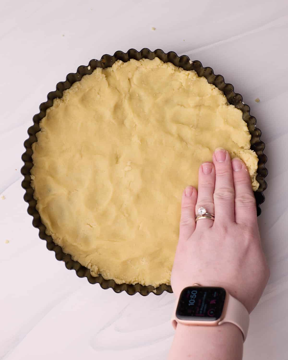 Pressing shortbread crust dough into the base of a tart pan.