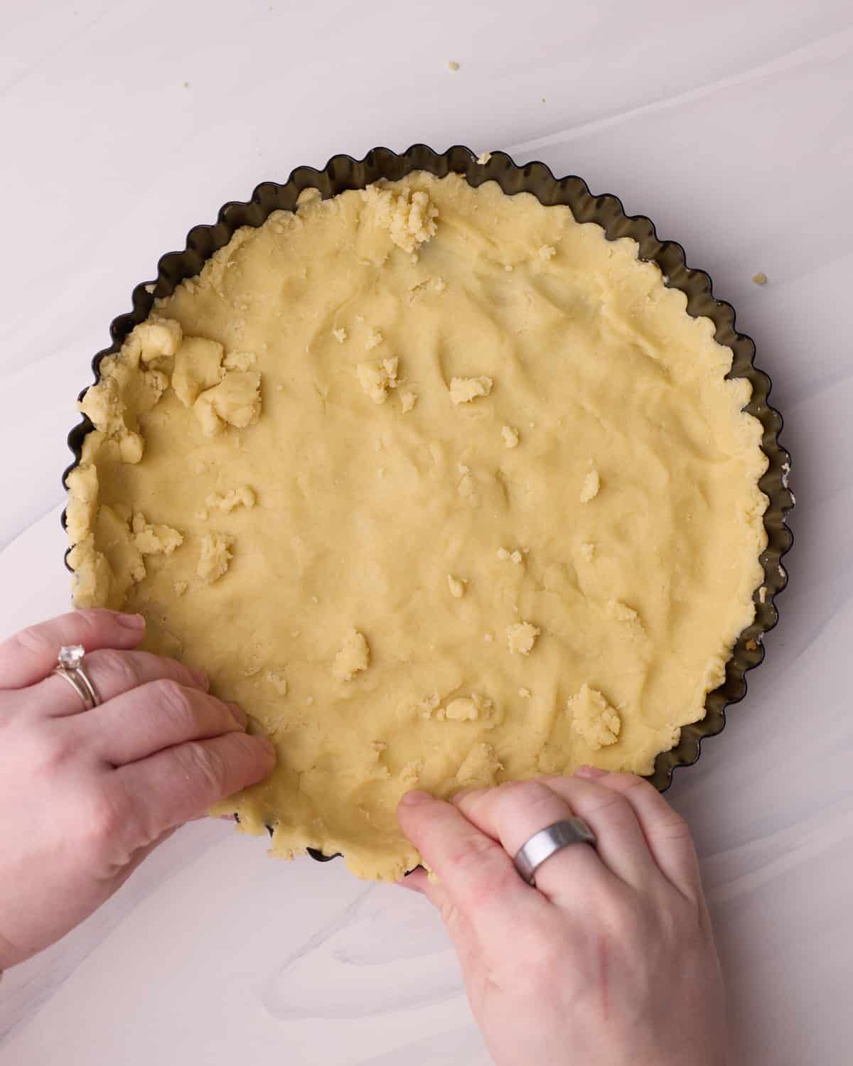 Using hands to press shortbread tart dough into the sides of a tart pan.
