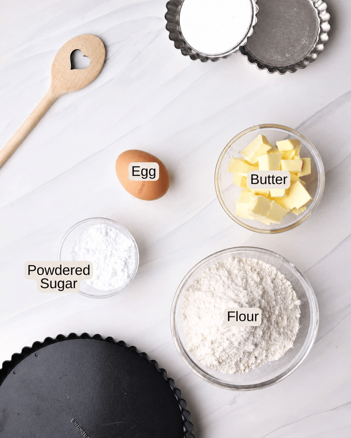 Ingredients to make shortbread tart crust, including butter, flour, powdered sugar and an egg yolk.