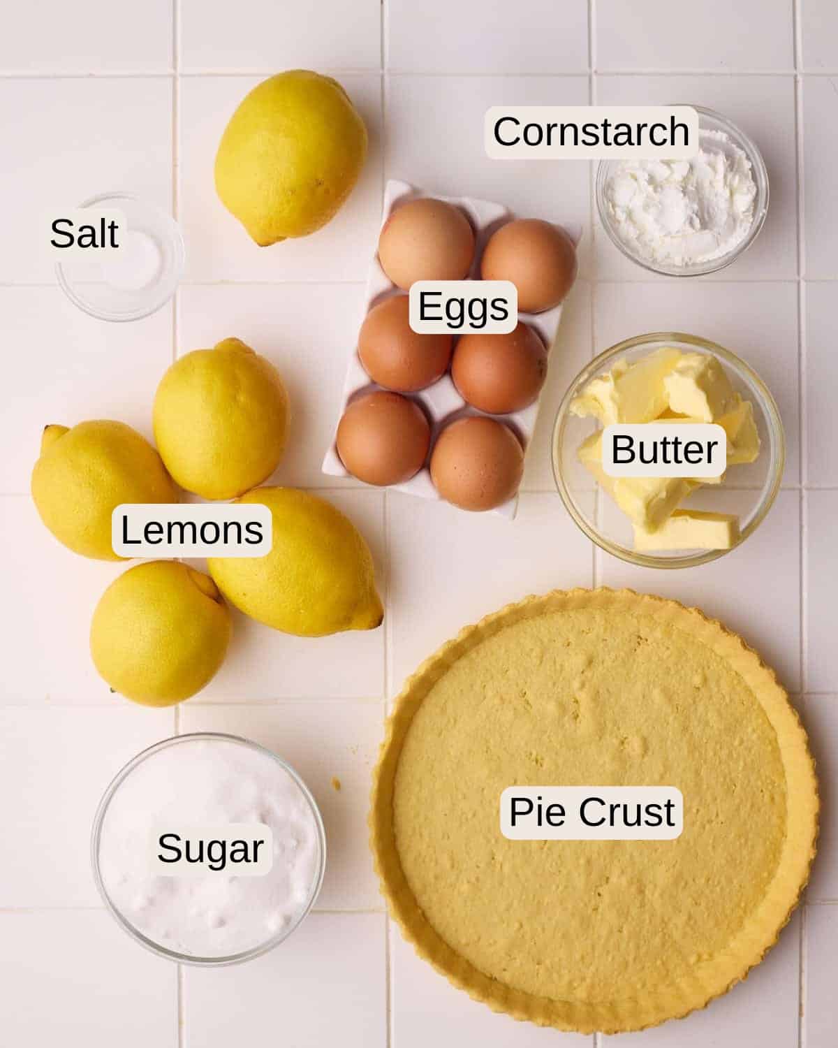 Ingredients to make lemon meringue pie including fresh lemons, pie crust, sugar, butter, eggs, cornstarch and salt.