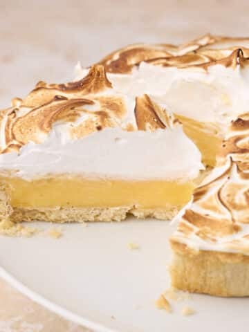 Lemon meringue pie with swiss meringue, with a slice being taken out of it to show the silky lemon filling.