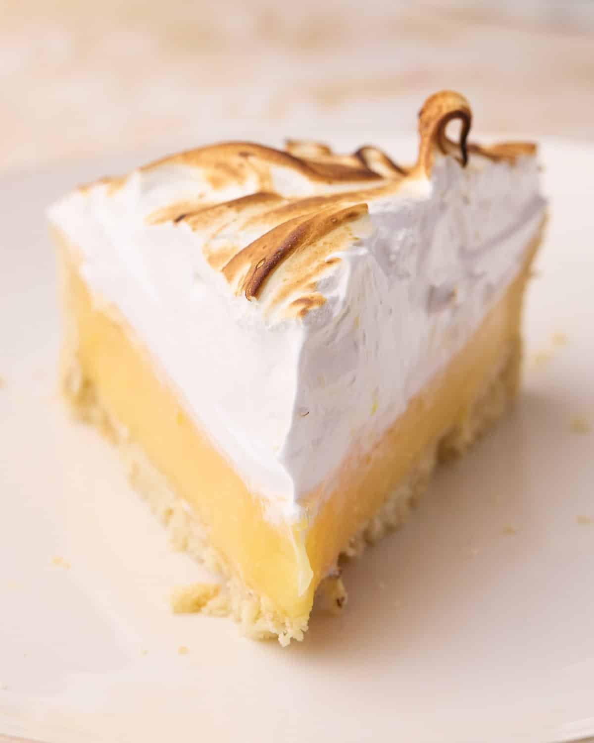 Super clean slice of lemon meringue pie shot from the front so you can see the sharp edges of lemon filling and swiss meringue.