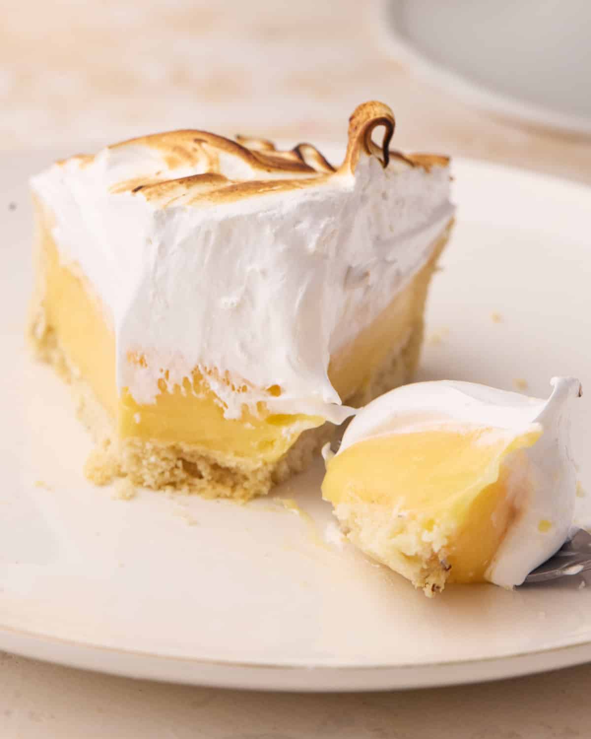 Slice of lemon meringue pie with a forkful taken out of it to show the silky lemon filling and marshmallowy toasted meringue on top. 