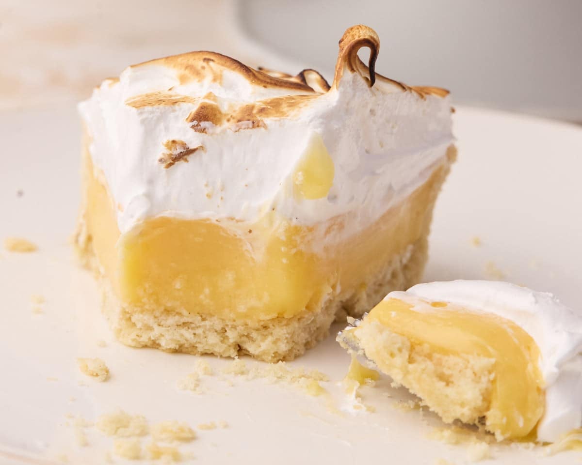 Slice of lemon meringue pie with a forkful taken out of it to show the silky lemon filling and marshmallowy toasted meringue on top.
