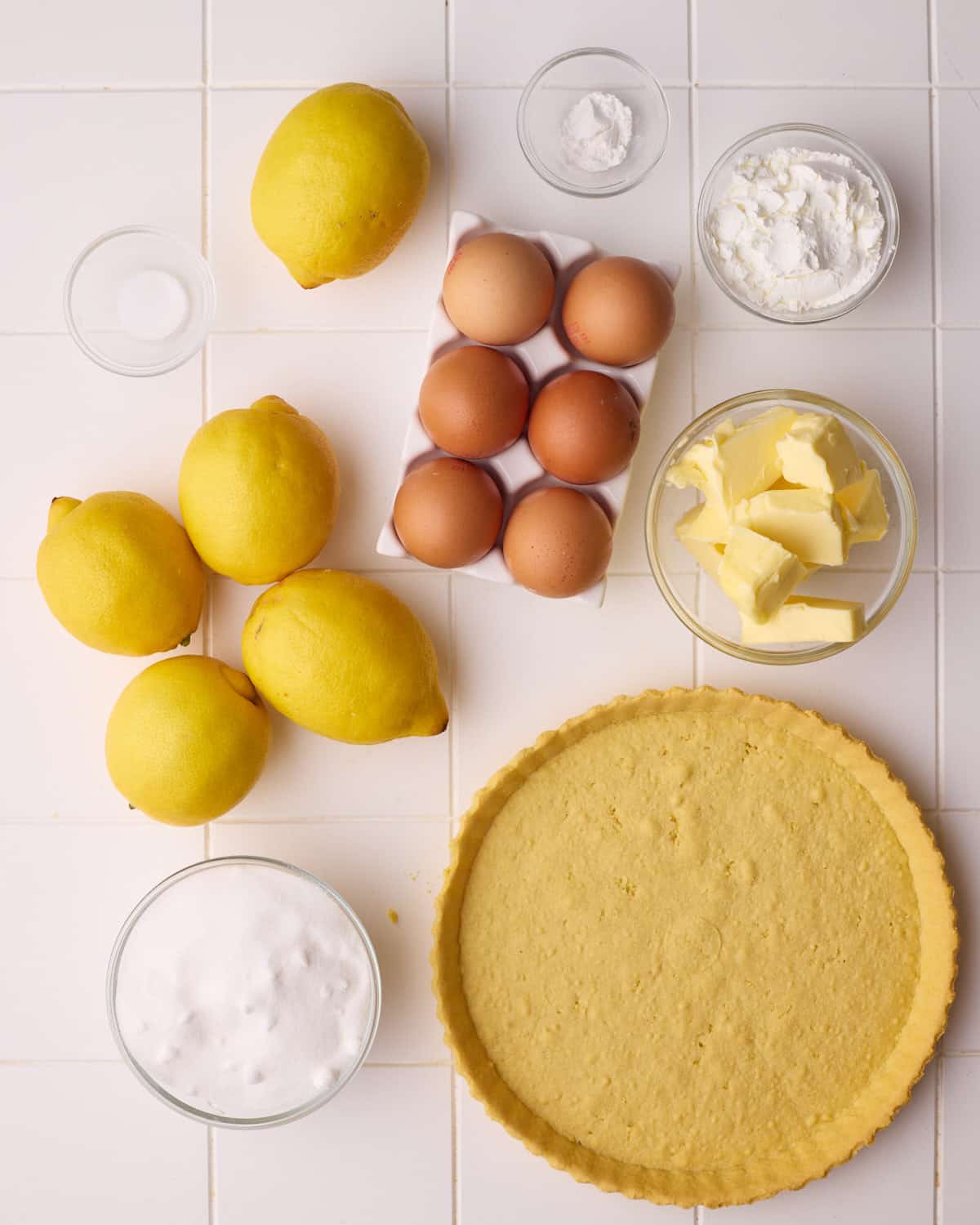 Ingredients to make lemon meringue pie including fresh lemons, pie crust, sugar, butter, eggs, cornstarch and salt.