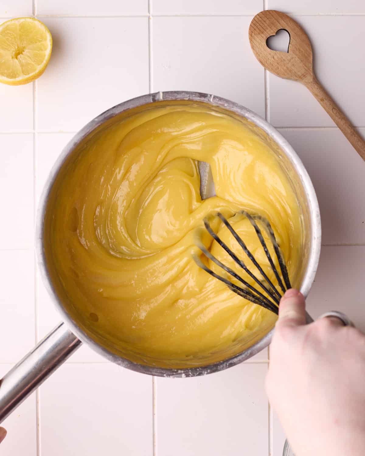 Lemon filling in a saucepan being whisked until glossy and smooth.