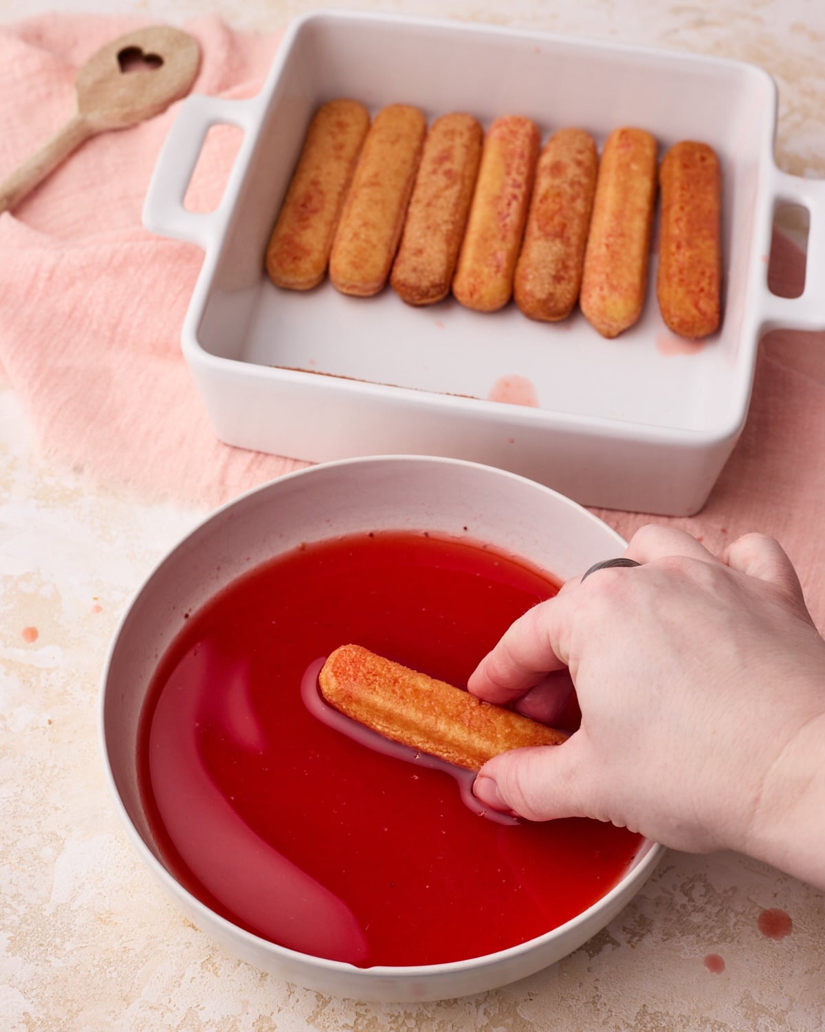 Process picture showing ladyfingers being dipped into strawberry simple syrup to make strawberry tiramisu.