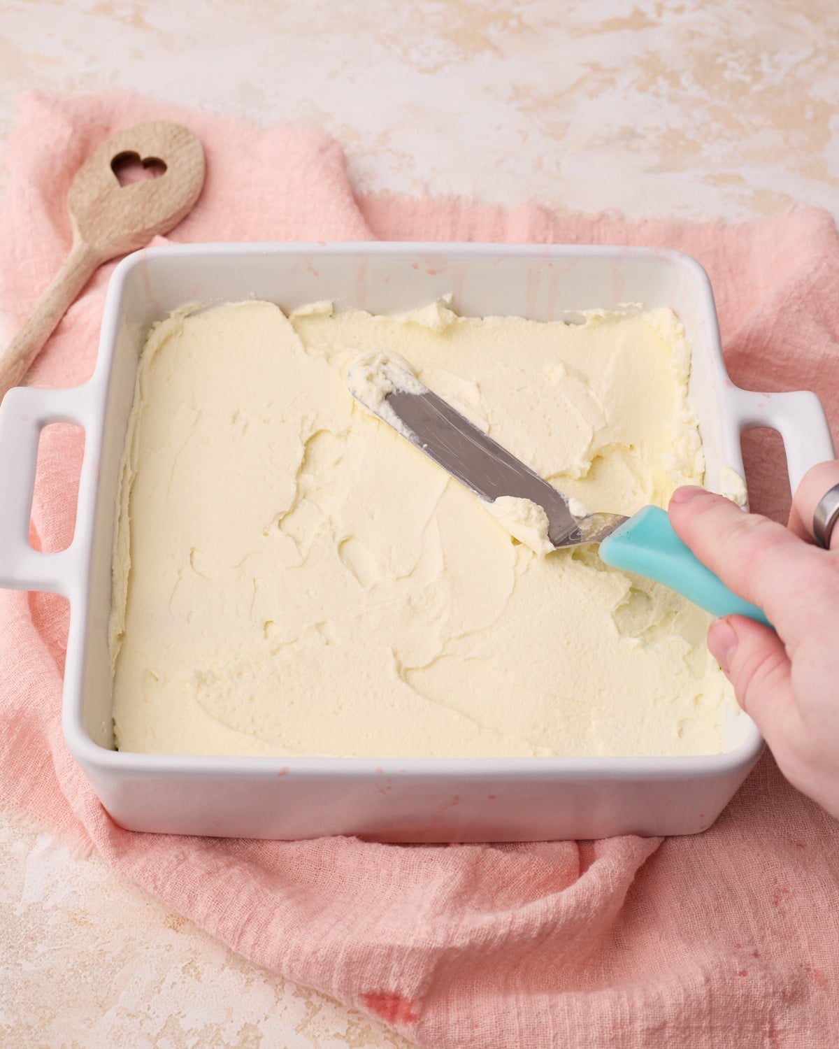 Mascarpone cream being spread out evenly on top of soaked ladyfingers to make strawberry tiramisu.