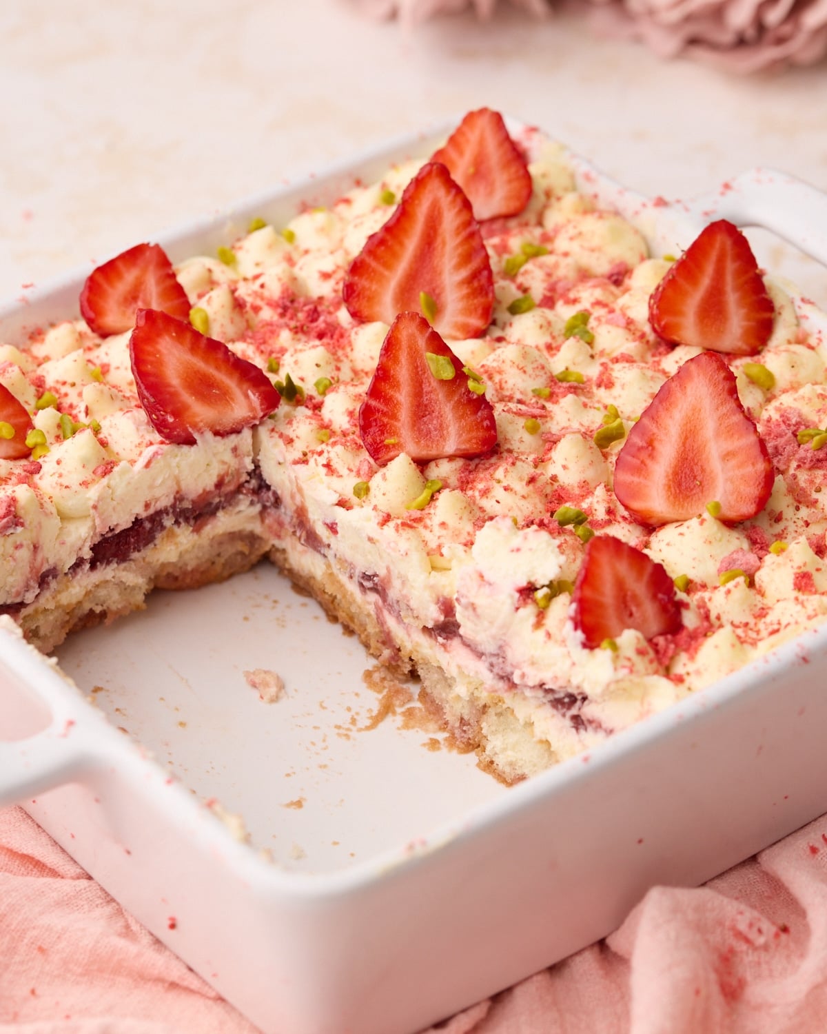 Strawberry tiramisu in a square baking dish with a few slices cut out to show the layers inside of strawberry soaked ladyfingers, mascarpone cream and strawberries.