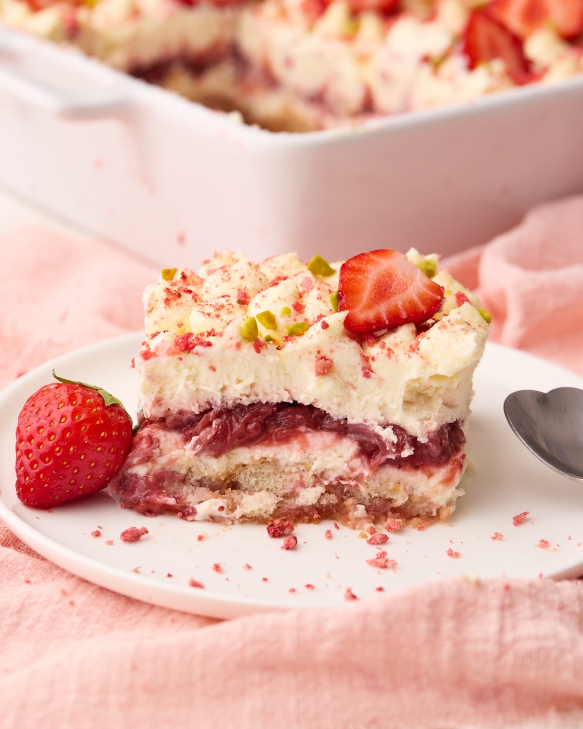 Slice of strawberry tiramisu layered dessert on a plate showing all the layers inside of strawberry syrup soaked ladyfingers and mascarpone cream.