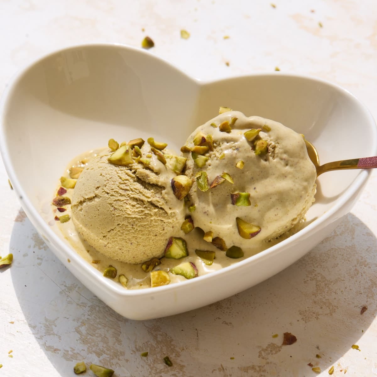 Two scoops of homemade pistachio ice cream in a bowl in the sun with chopped pistachios sprinkled on top.