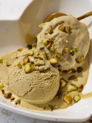 Two scoops of homemade pistachio ice cream in a bowl with chopped pistachios sprinkled on top.