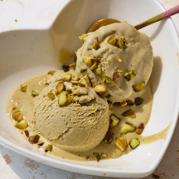 Two scoops of homemade pistachio ice cream in a bowl with chopped pistachios sprinkled on top.