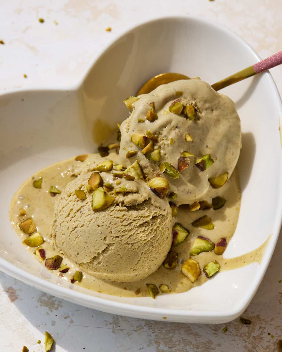 Two scoops of homemade pistachio ice cream in a bowl with chopped pistachios sprinkled on top.